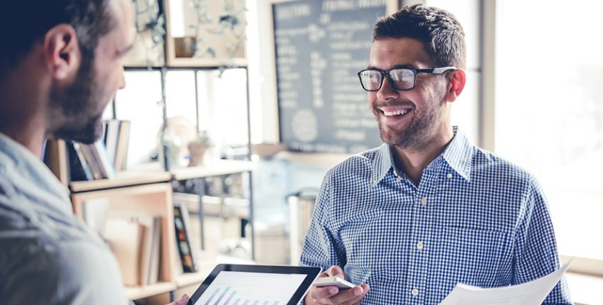 Handsome businessmen are using gadgets, talking and smiling while working in office